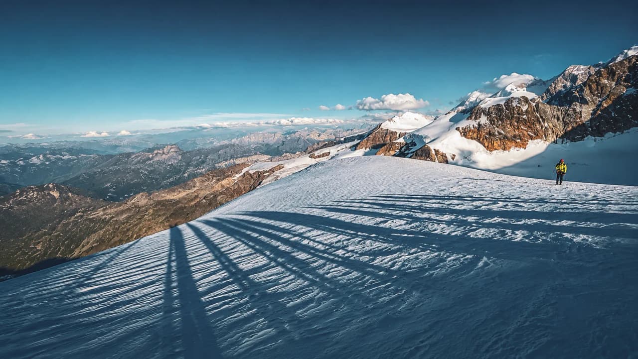 Een bergbeklimmer steekt af tegen een gletsjer, te midden van majestueuze landschappen met besneeuwde bergen.