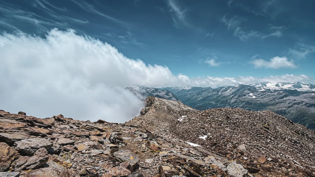 Panoramisch uitzicht vanaf een bergtop, met drijvende wolken en majestueuze bergen op de achtergrond.
