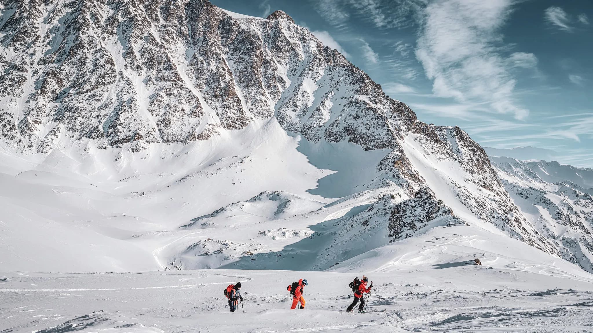 Trois randonneurs progressent sur la neige immaculée, entourés par des sommets majestueux.