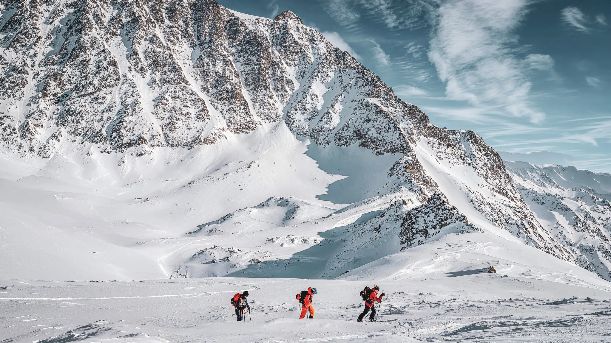 Trois randonneurs progressent sur la neige immaculée, entourés par des sommets majestueux.