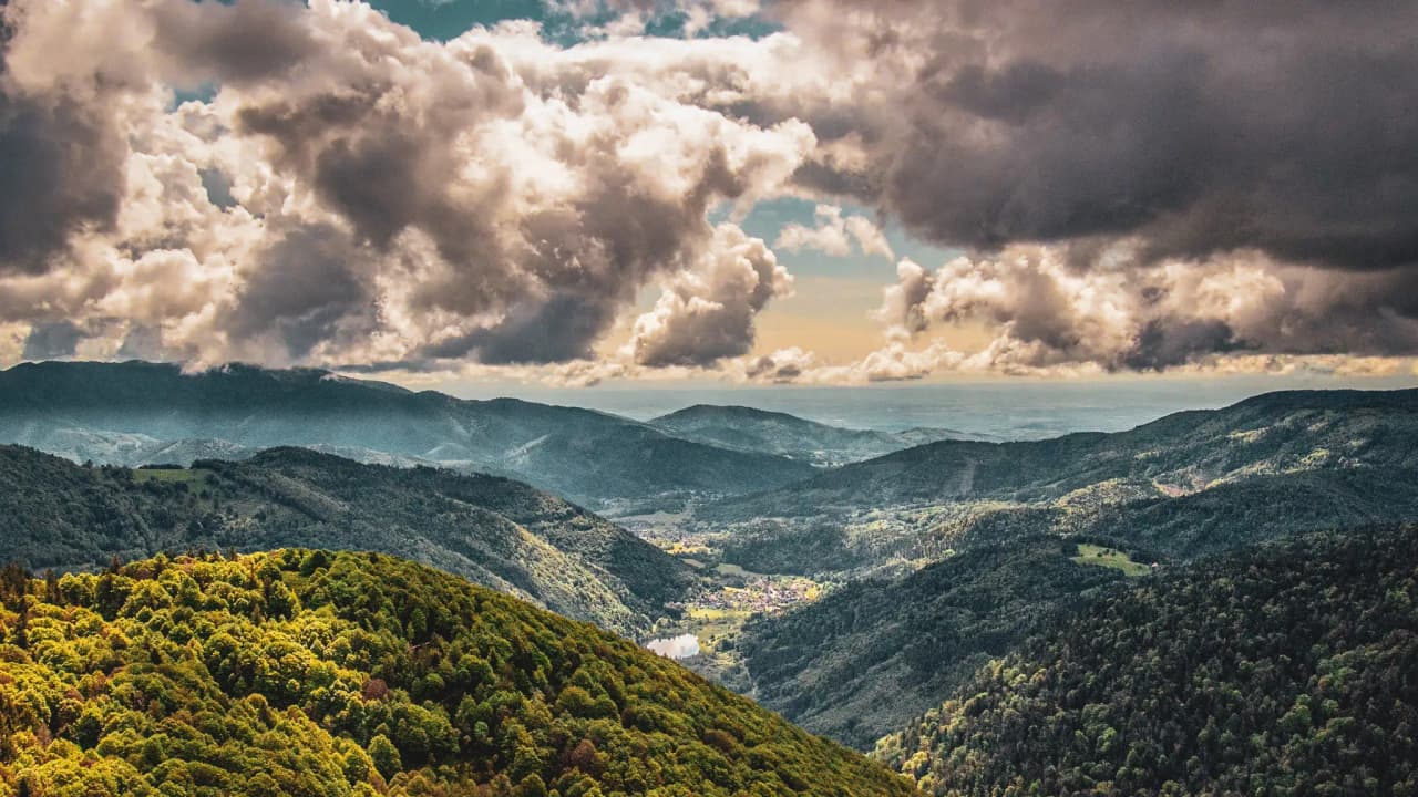 Vaste panorama des Vosges, avec des vallées verdoyantes sous un ciel nuageux majestueux.