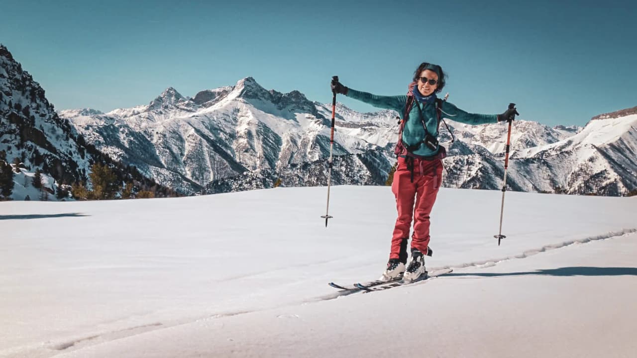 Skieuse de randonnée souriante face aux montagnes enneigées du Mont Viso, ambiance énergique et aventureuse.