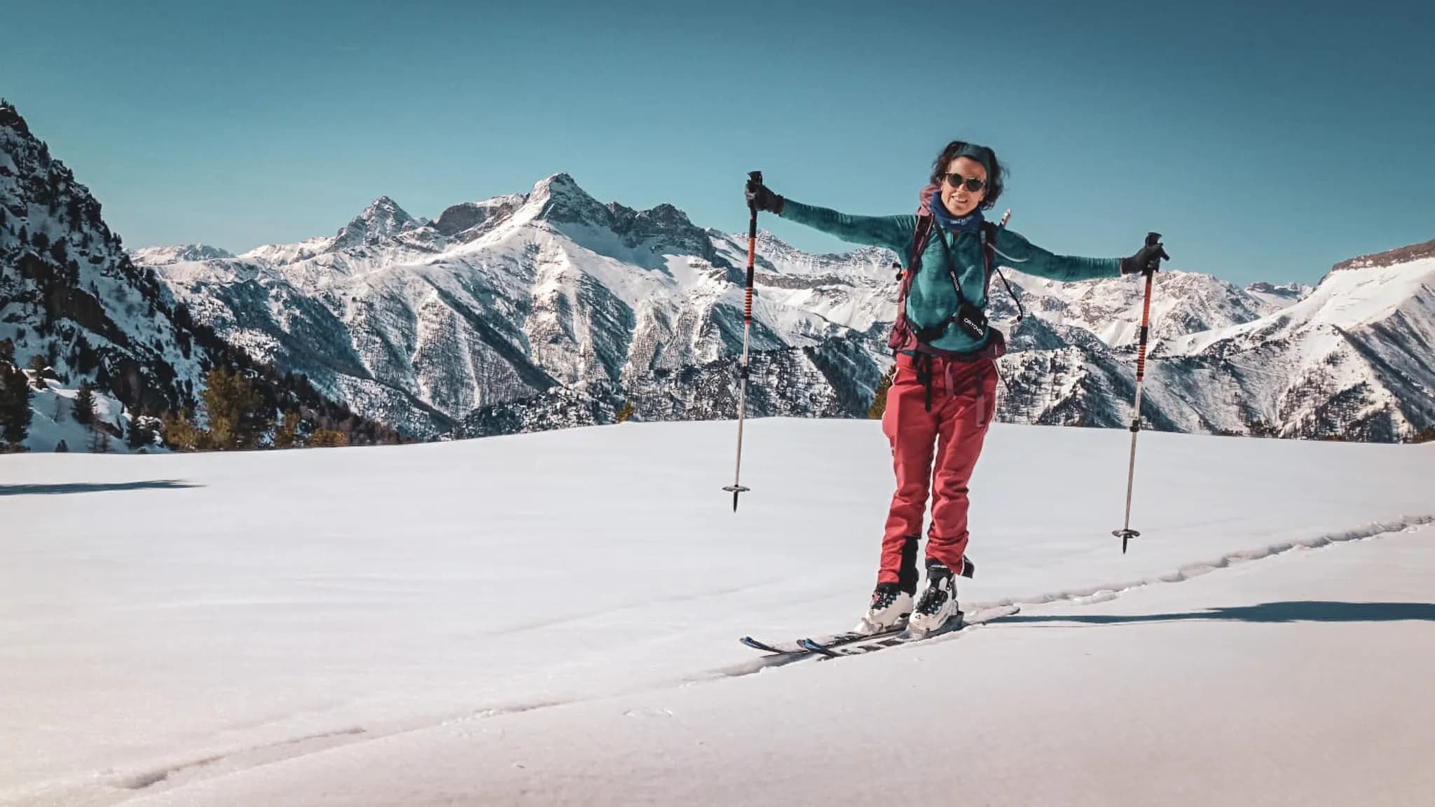 Skieuse de randonnée souriante face aux montagnes enneigées du Mont Viso, ambiance énergique et aventureuse.
