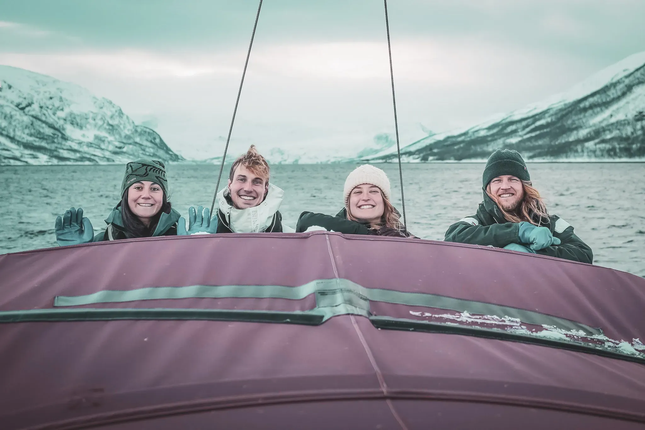 Four smiling friends on a boat, surrounded by the spectacular snowy scenery of the Lyngen Alps.