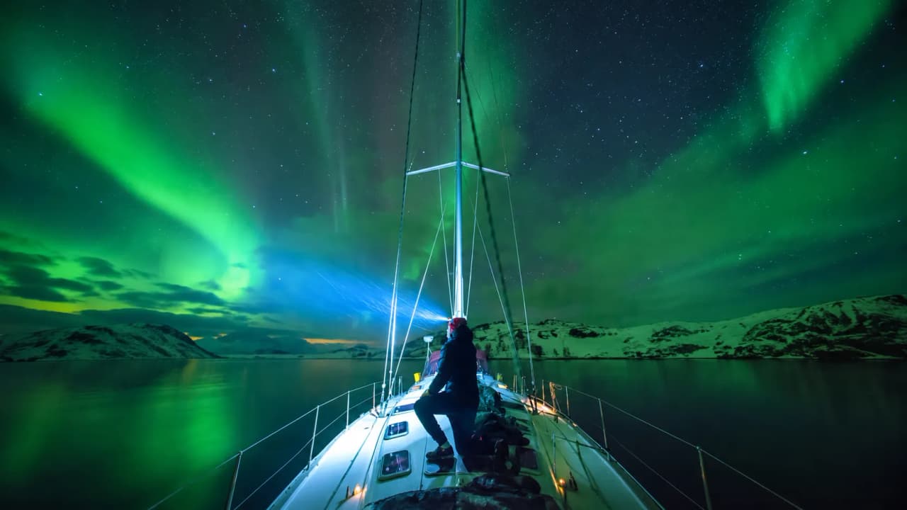 Sailor enjoying the northern lights over the tranquil waters of Lyngen Alps, Norway.