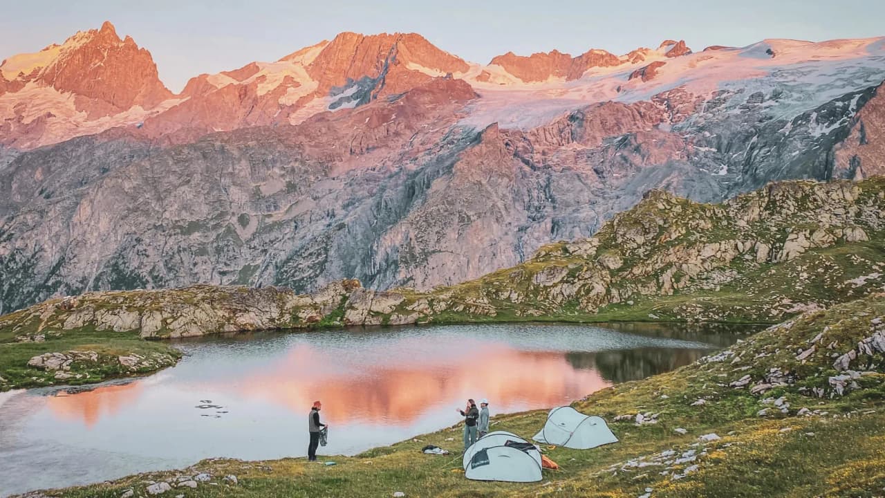 Un bivouac enchanteur au bord d'un lac, entouré de sommets majestueux illuminés par le coucher de soleil.