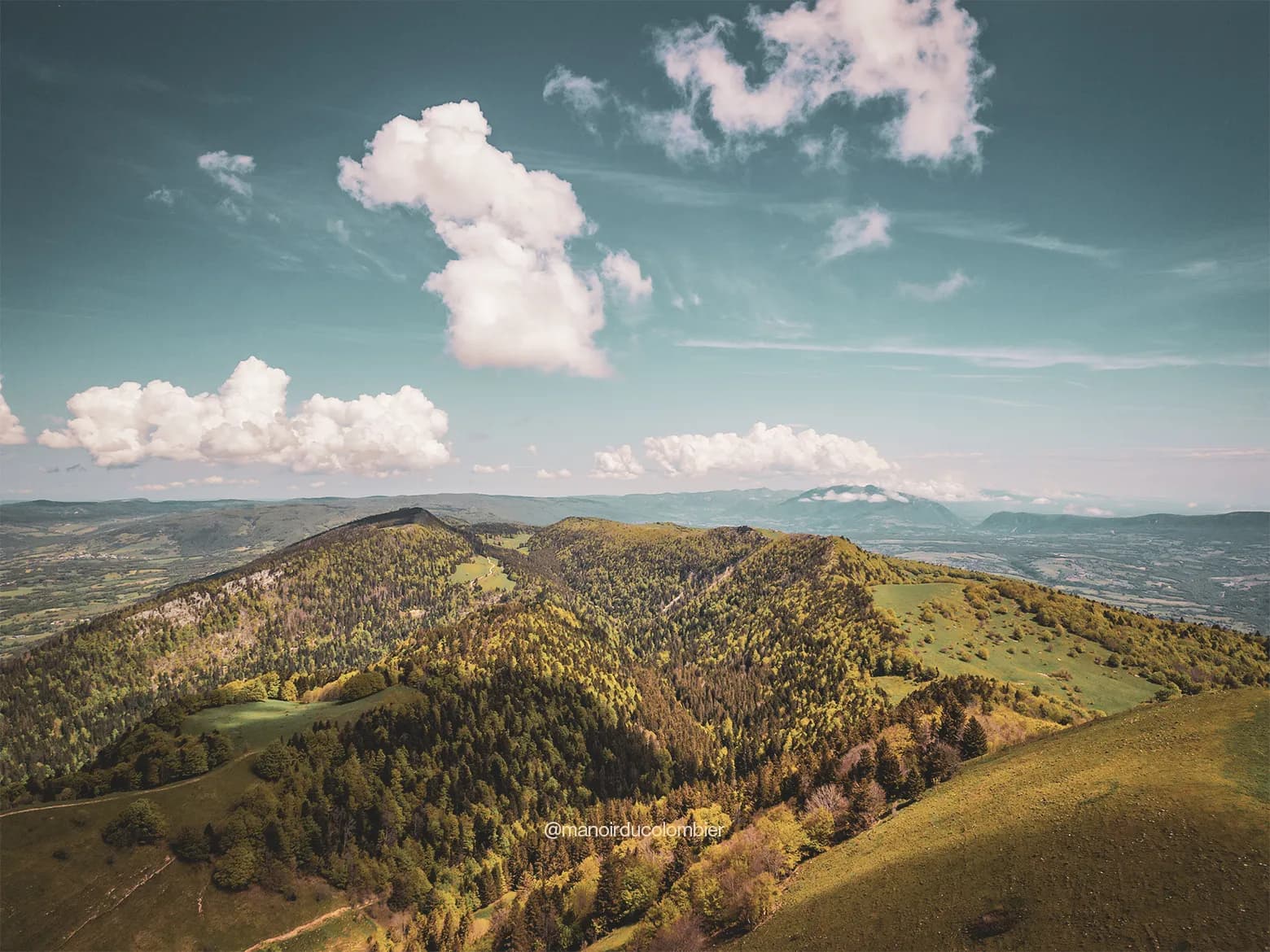 Vue panoramique du Grand Colombier, verdure luxuriante et nuages dans un ciel bleu. Évasion nature garantie !