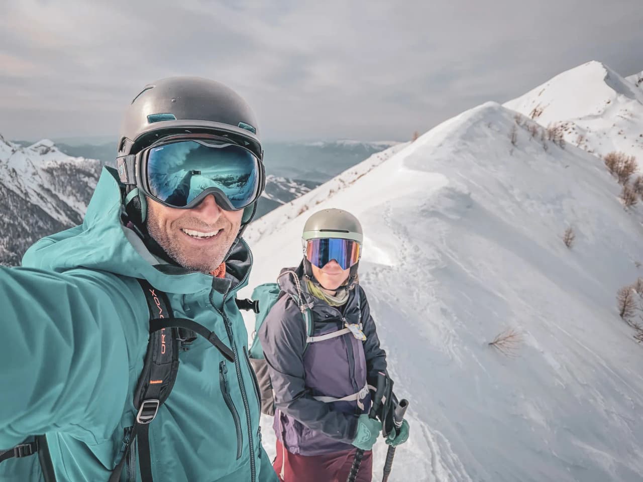 Ski touring in the Écrins: smiling skiers on a snow-covered peak beneath a clear sky.