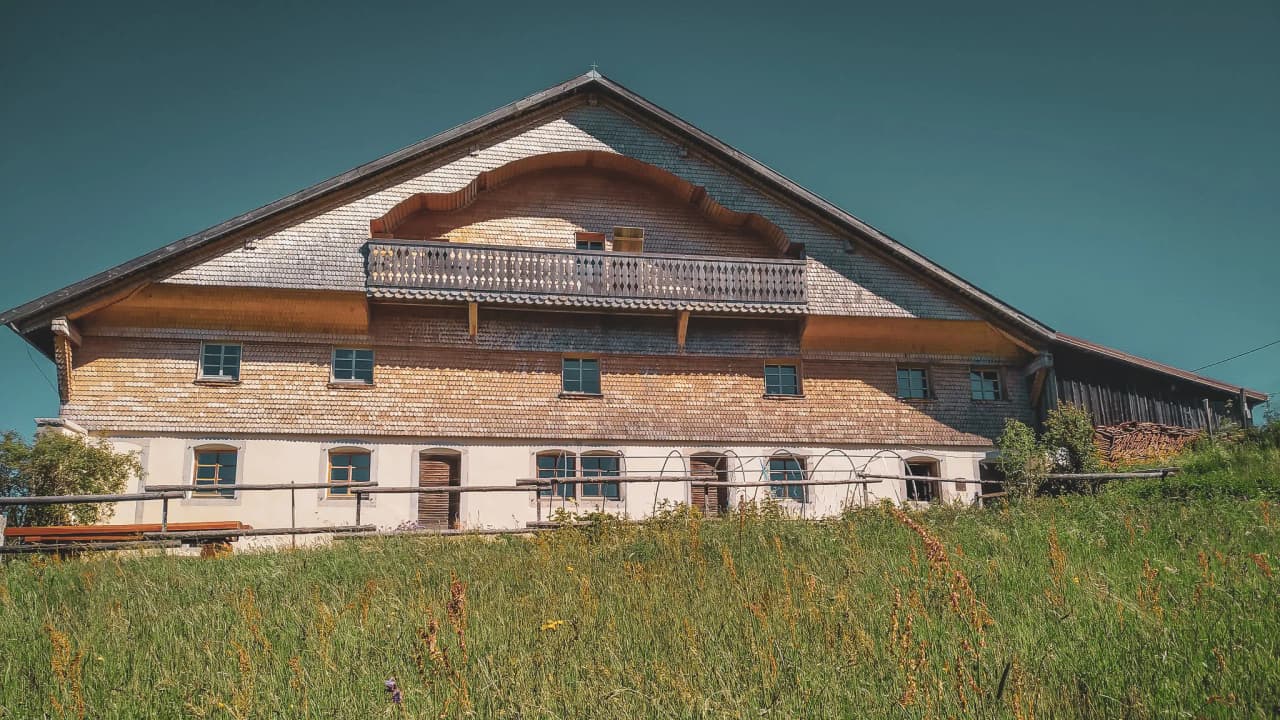 A picturesque chalet in the Jura, surrounded by greenery and under a brilliant blue sky.