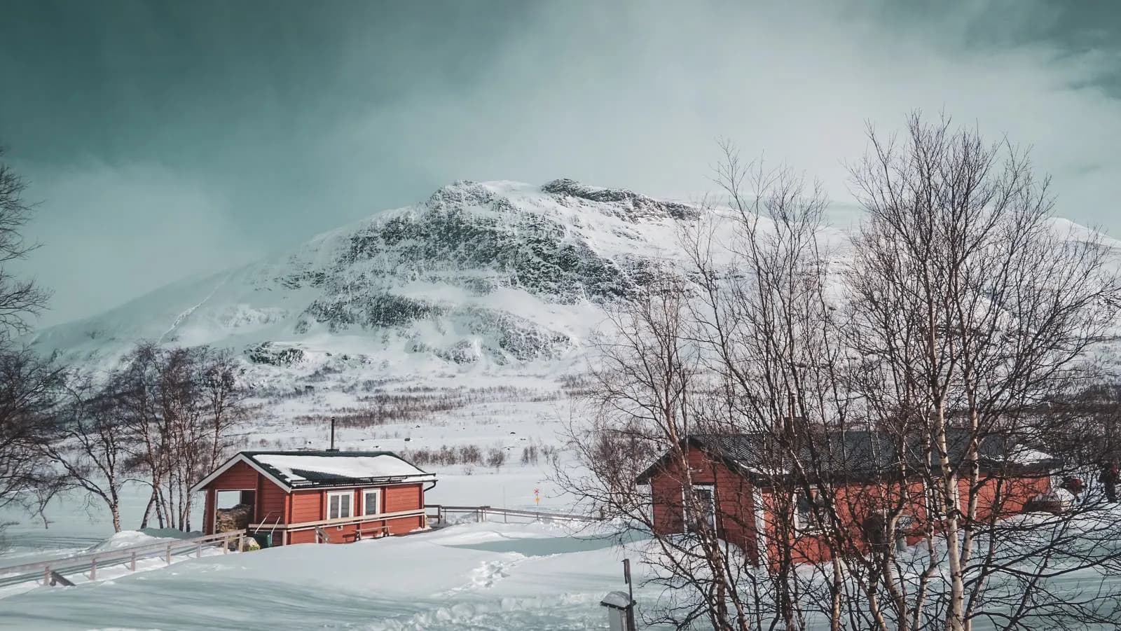 Red cabins at the foot of a snow-capped mountain under a turquoise sky, an invitation to adventure in Lapland.