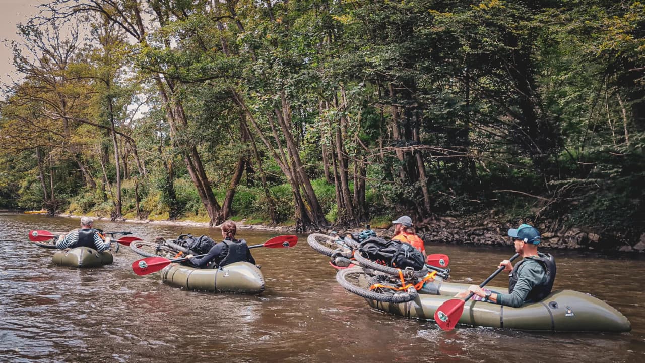 Adventurers enjoy the river Lesse in packraft, surrounded by lush green countryside.