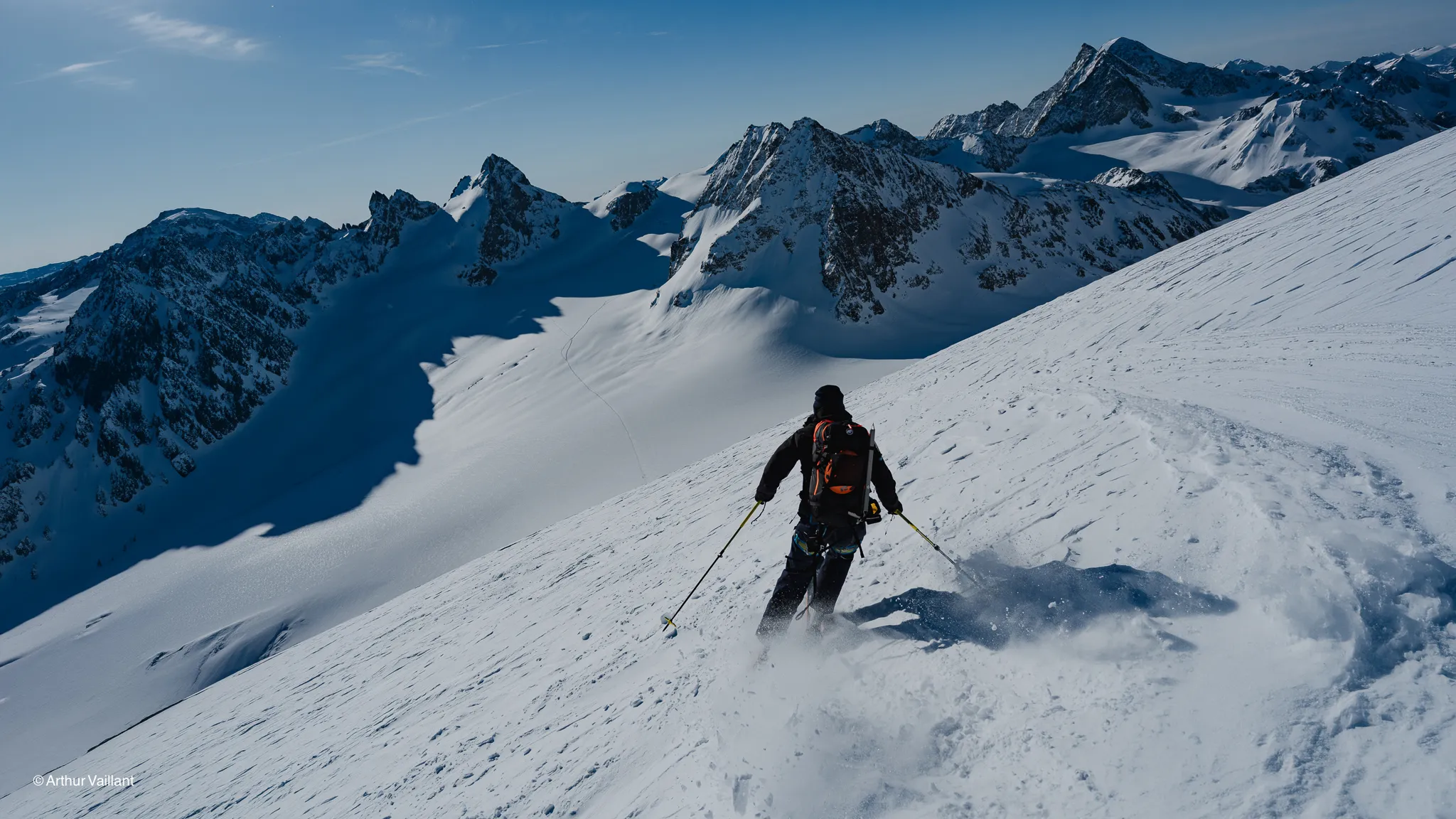 A skier on a sun-drenched slope, with majestic mountains and glistening glaciers in the background.