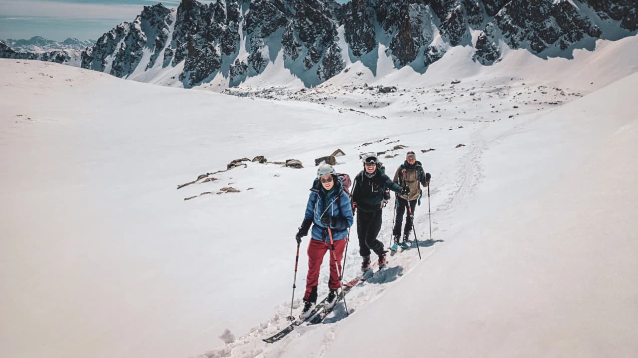Trois skieurs de randonnée traversent un paysage enneigé, avec un panorama majestueux de montagnes.