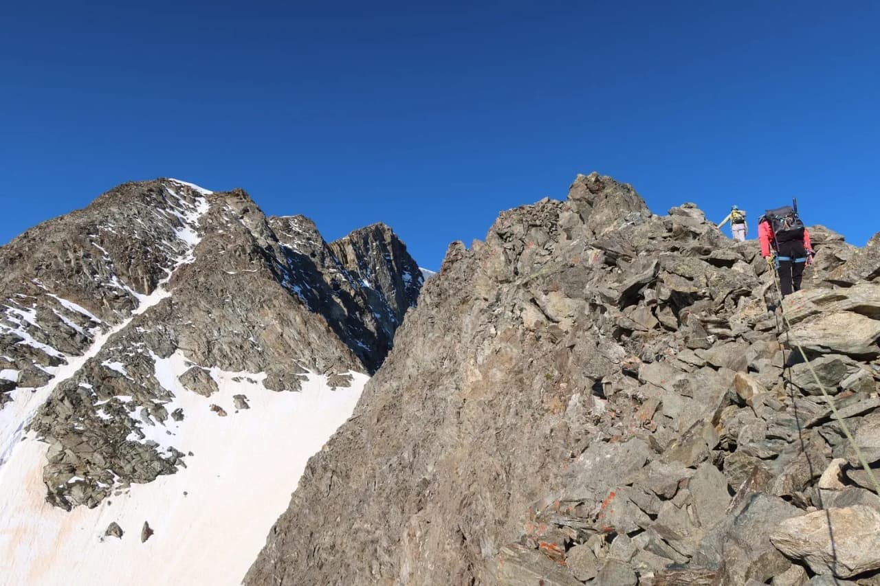 A group of hikers climbing a rocky ridge facing Mont Blanc under a brilliant sky.