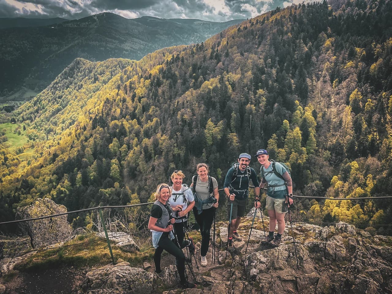A group of hikers on a summit, admiring a green panorama of the Vosges mountains.