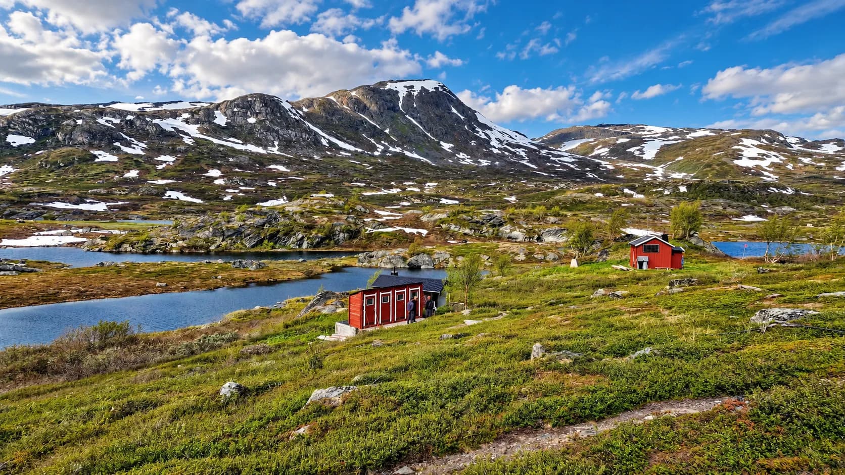 Een idyllisch landschap in Zweeds Lapland: majestueuze bergen, glinsterende meren en pittoreske rode hutten.