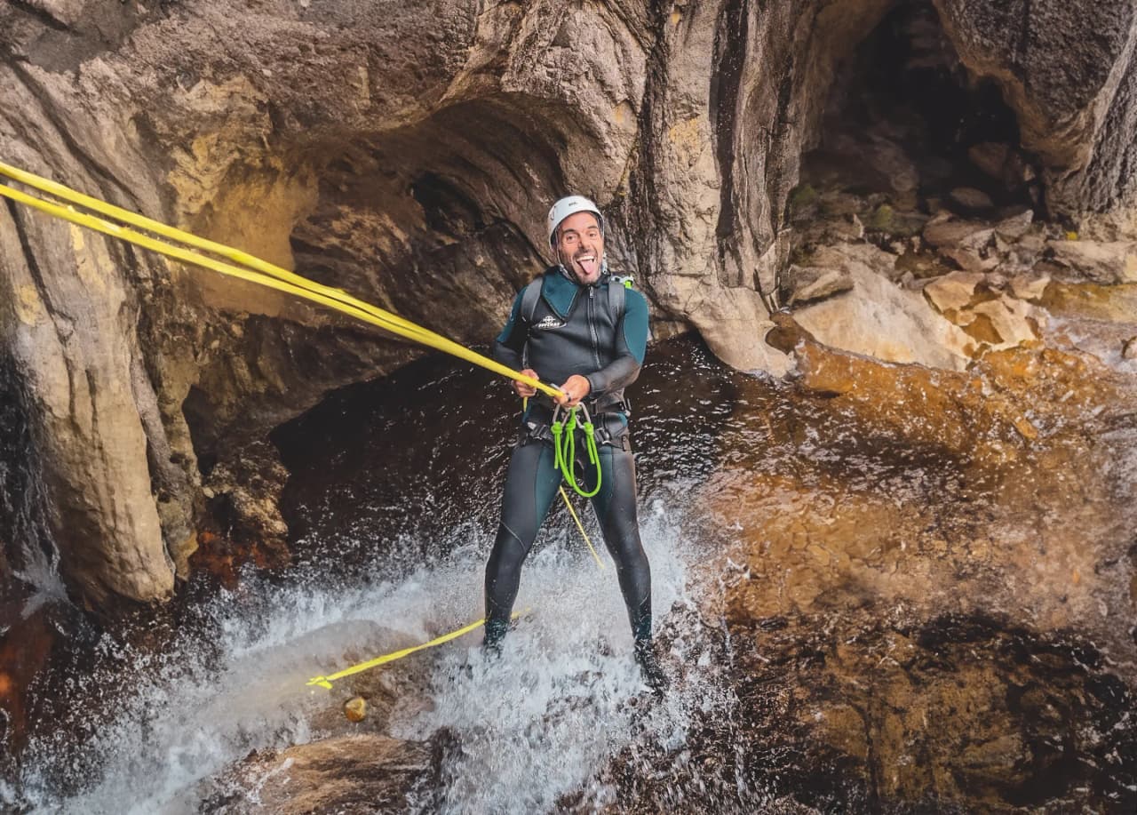 Un aventurier en combinaison de plongée descend en rappel dans un canyon turquoise, entouré de roches.