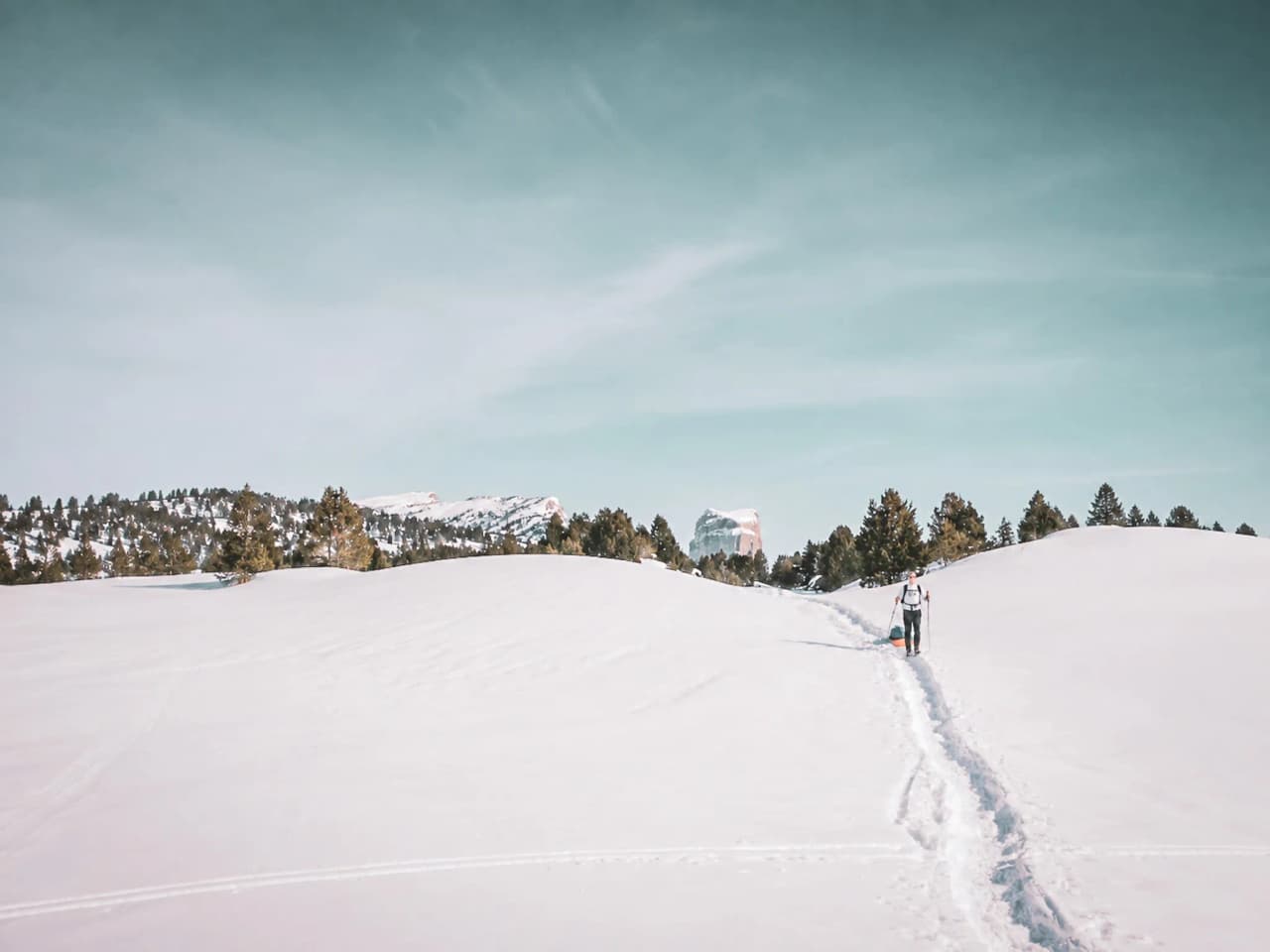Een avonturier die een pulka over de sneeuw trekt, met de bergen op de achtergrond.