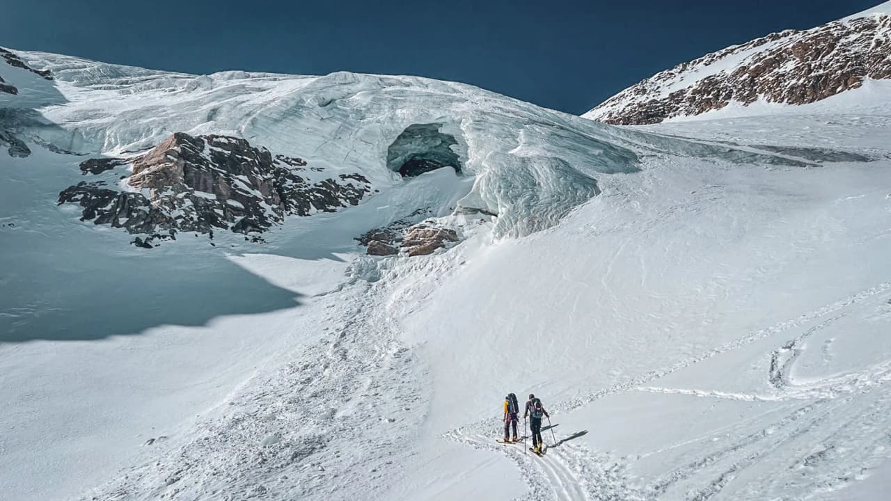 Two ski-tourers make their way across an immaculate glacier, a majestic Alpine landscape.