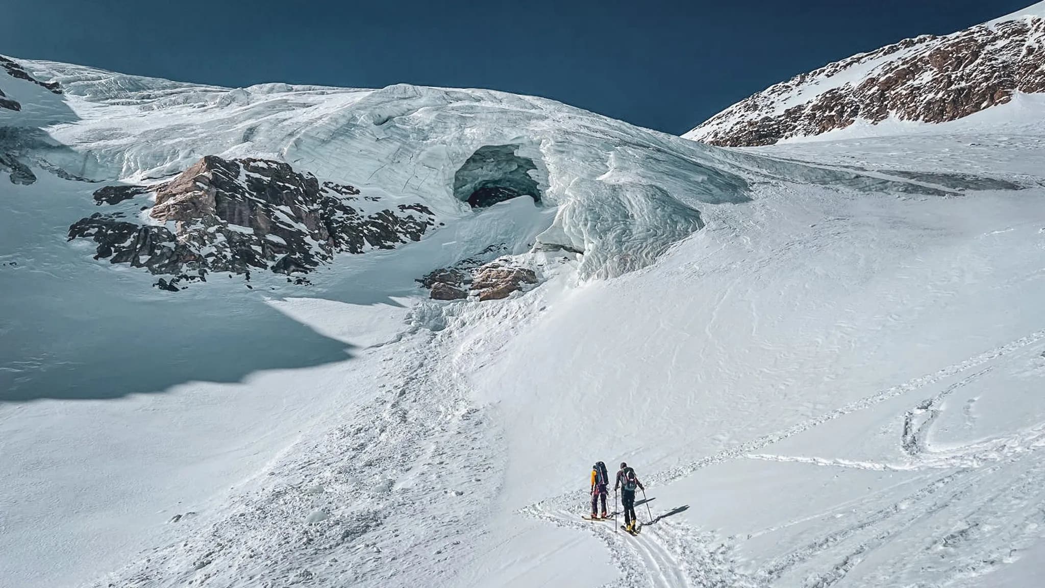 Deux skieurs de randonnée progressent sur un glacier immaculé, majestueux paysage alpin.