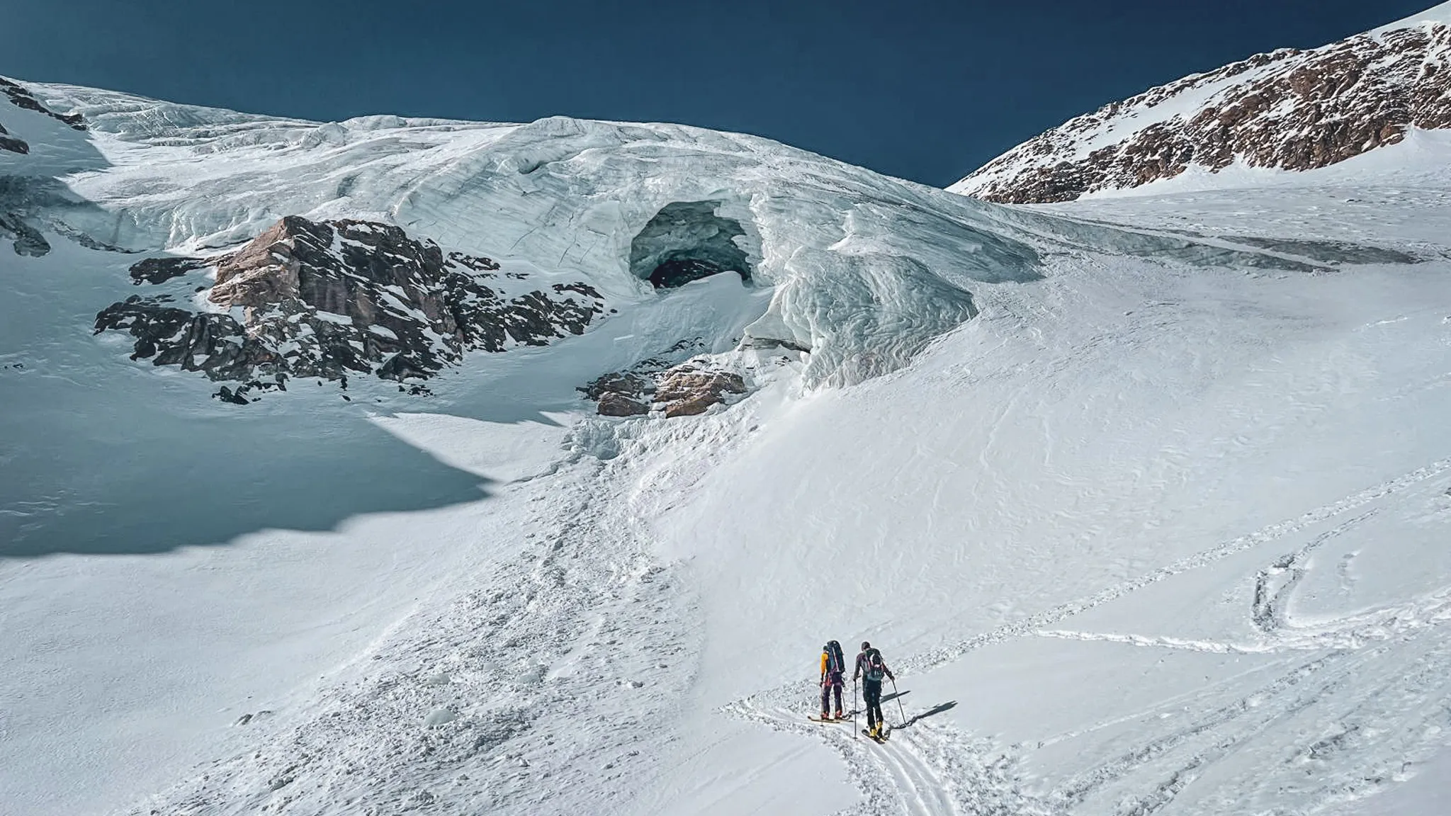 Deux skieurs de randonnée progressent sur un glacier immaculé, majestueux paysage alpin.