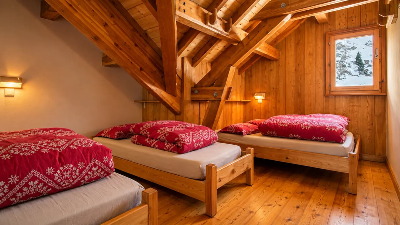 A cosy wooden room, with snug beds and red blankets, and a view of the snow-capped mountains.
