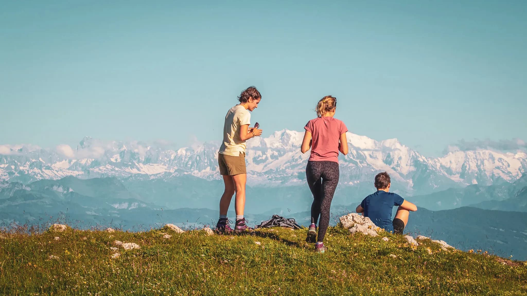 A group of hikers admiring the snow-capped Jura mountains under a sunny sky.