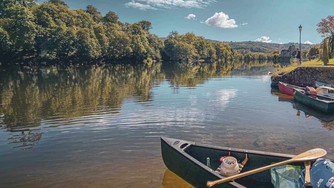Canoë sur l'eau calme de la Dordogne, entouré de forêts verdoyantes et d'un ciel serein.