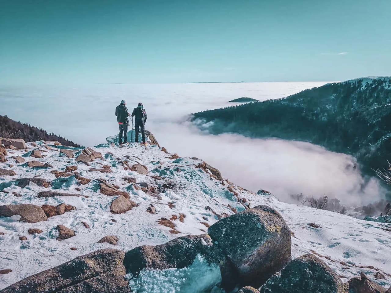 Twee wandelaars bewonderen een besneeuwd panorama van de Vogezen, gehuld in wolken.