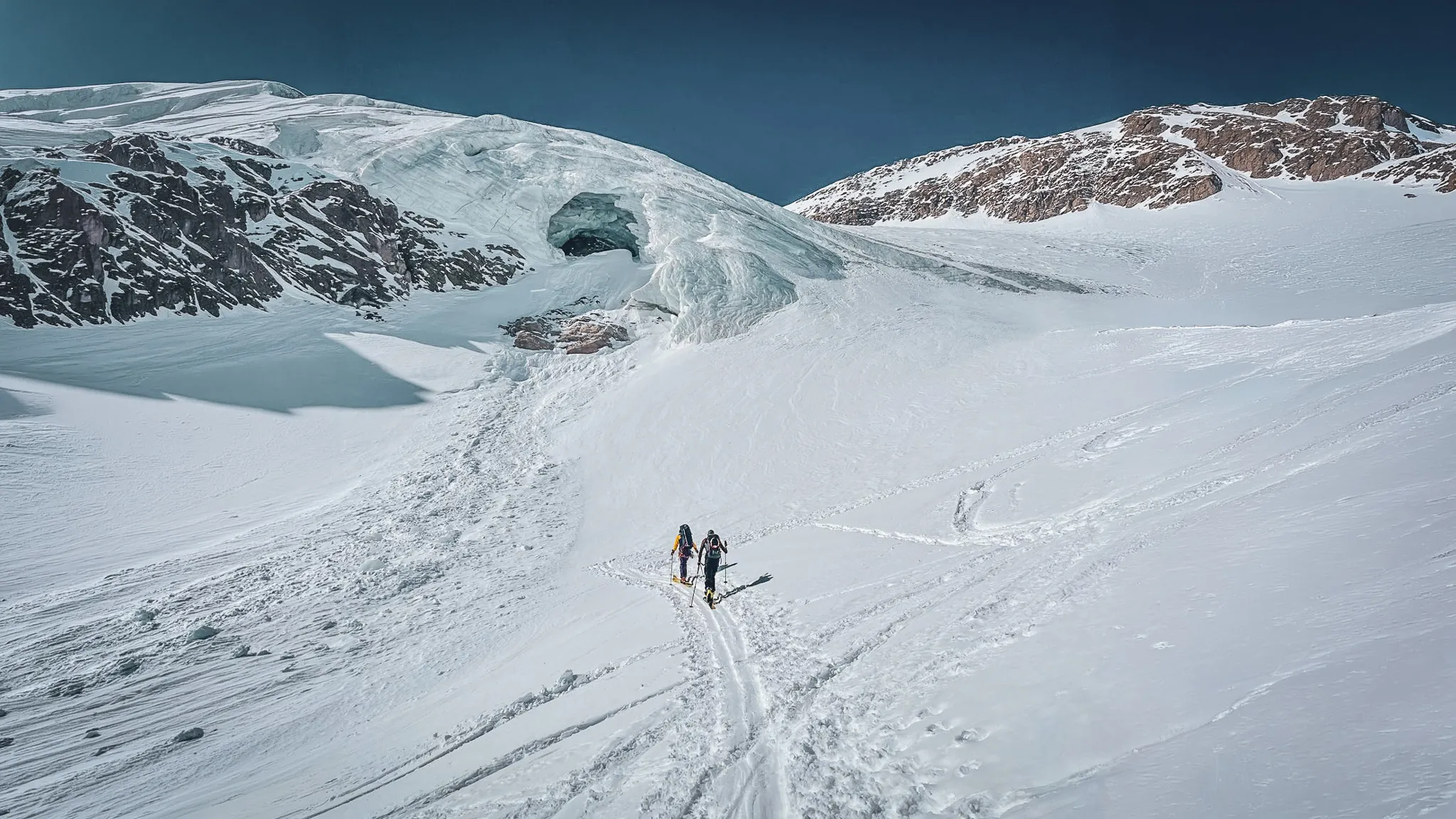 Groupe de skieurs traversant un glacier immaculé sous un ciel bleu, aventure en haute montagne.