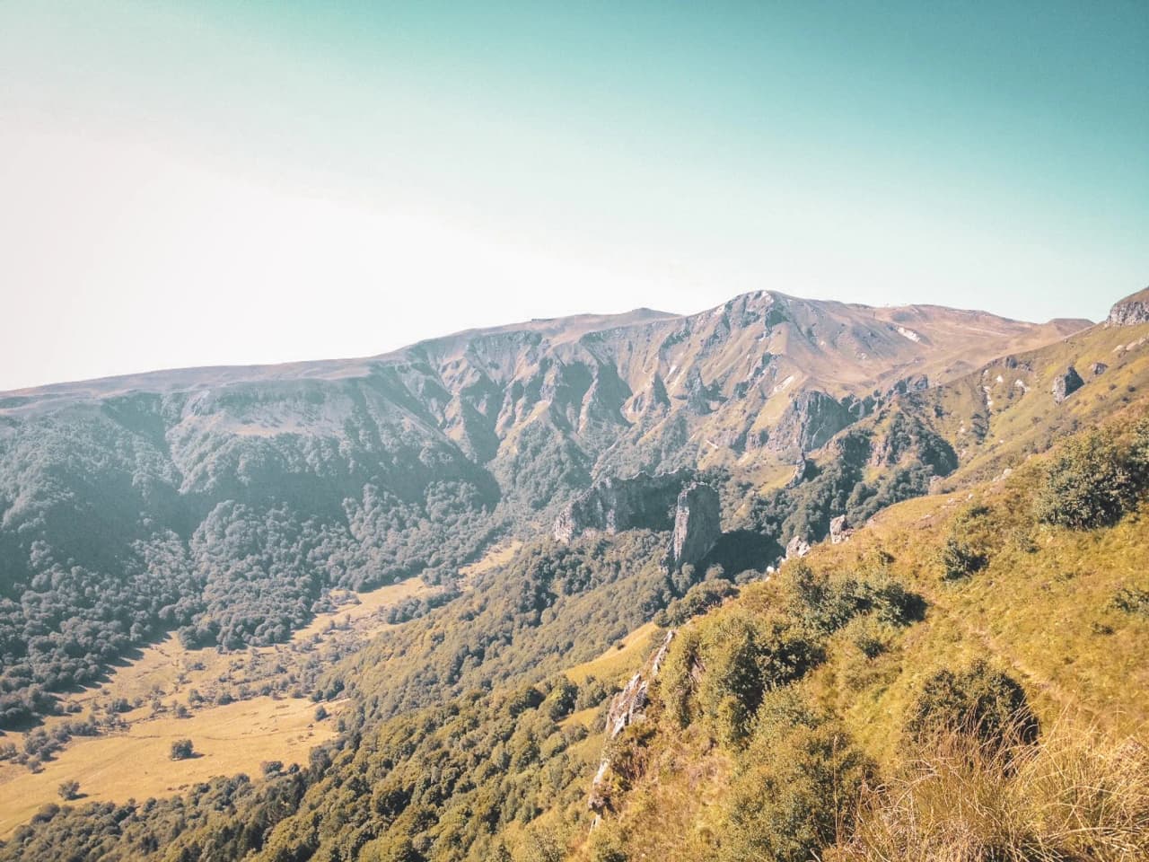 Een panoramisch uitzicht op de vulkaanruggen van het Centraal Massief, omgeven door groen en blauwe luchten.