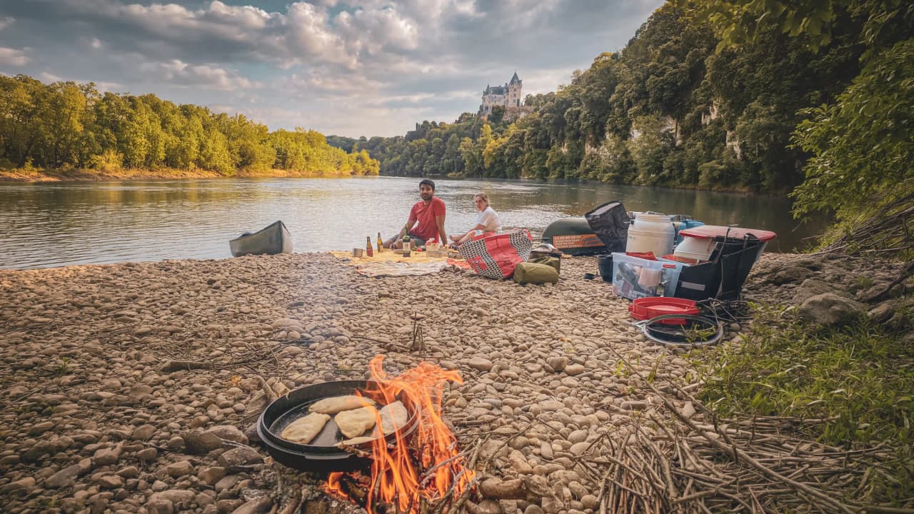 Un bivouac au bord de la Dordogne : feu de camp, canoë, repas en pleine nature sous un château.