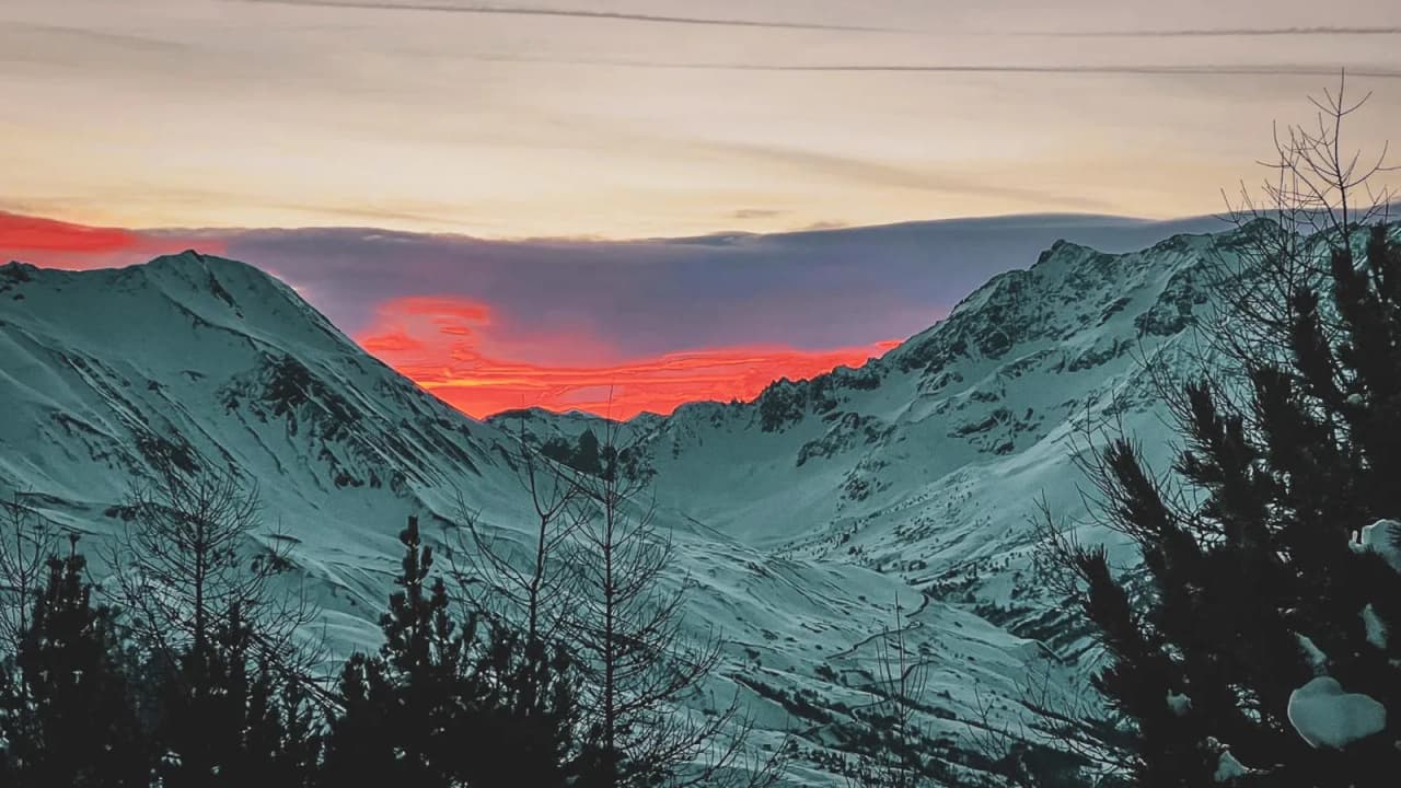 Een schitterende zonsondergang boven besneeuwde bergen, die je uitnodigt om te ontsnappen naar het hart van de natuur.