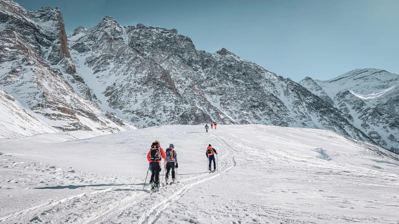 A group of ski tourers on a vast snowfield surrounded by majestic mountains.