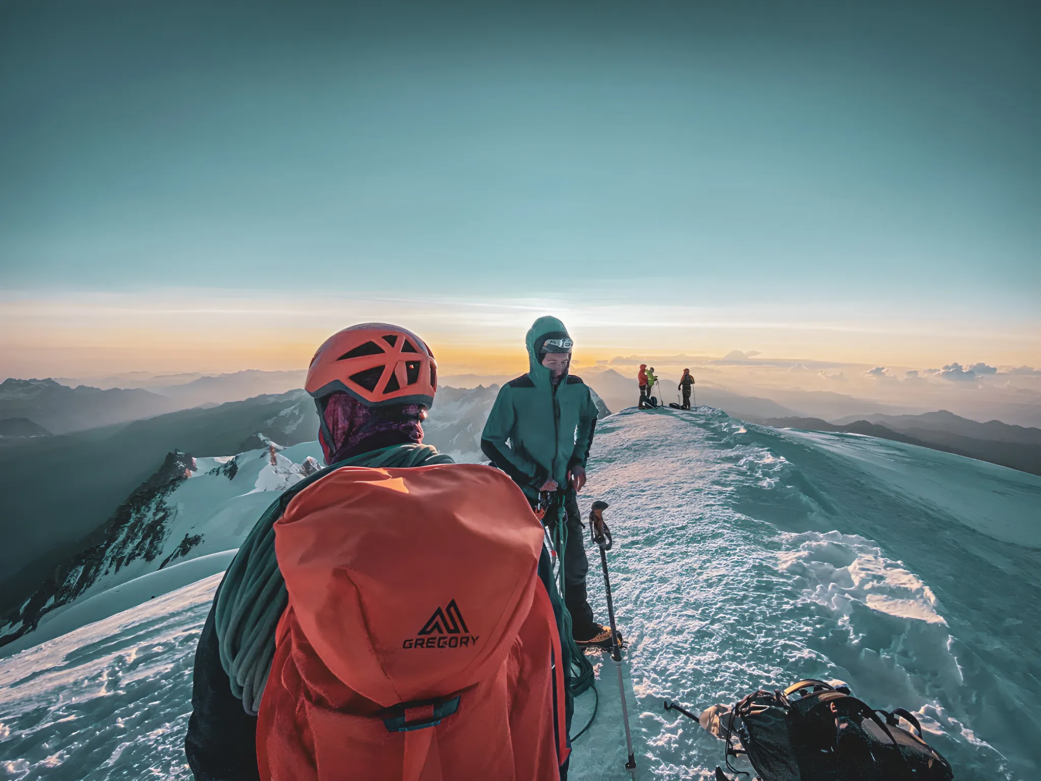 Groupe d'alpinistes au sommet du Mont Blanc, sous un ciel orange magique au coucher du soleil.