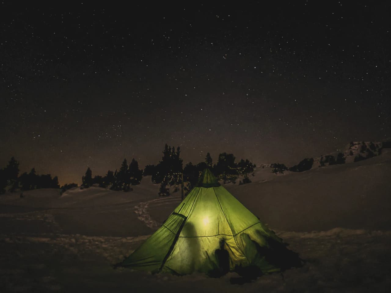 Een verlichte groene tipi onder een sterrenhemel, een sprookjesachtige sfeer in de sneeuw van de Vercors.