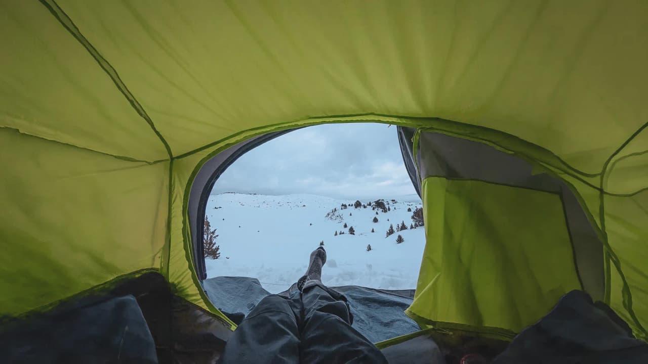 A view from a lit-up tent, looking out over a peaceful, wild snow-covered landscape. Perfect for an adventure!