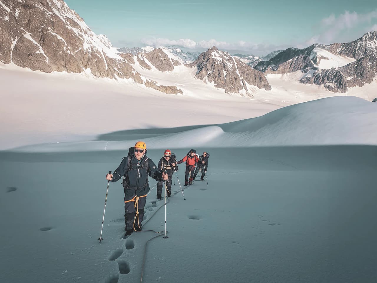 Group of climbers advancing on a glacier, surrounded by majestic Alpine peaks.