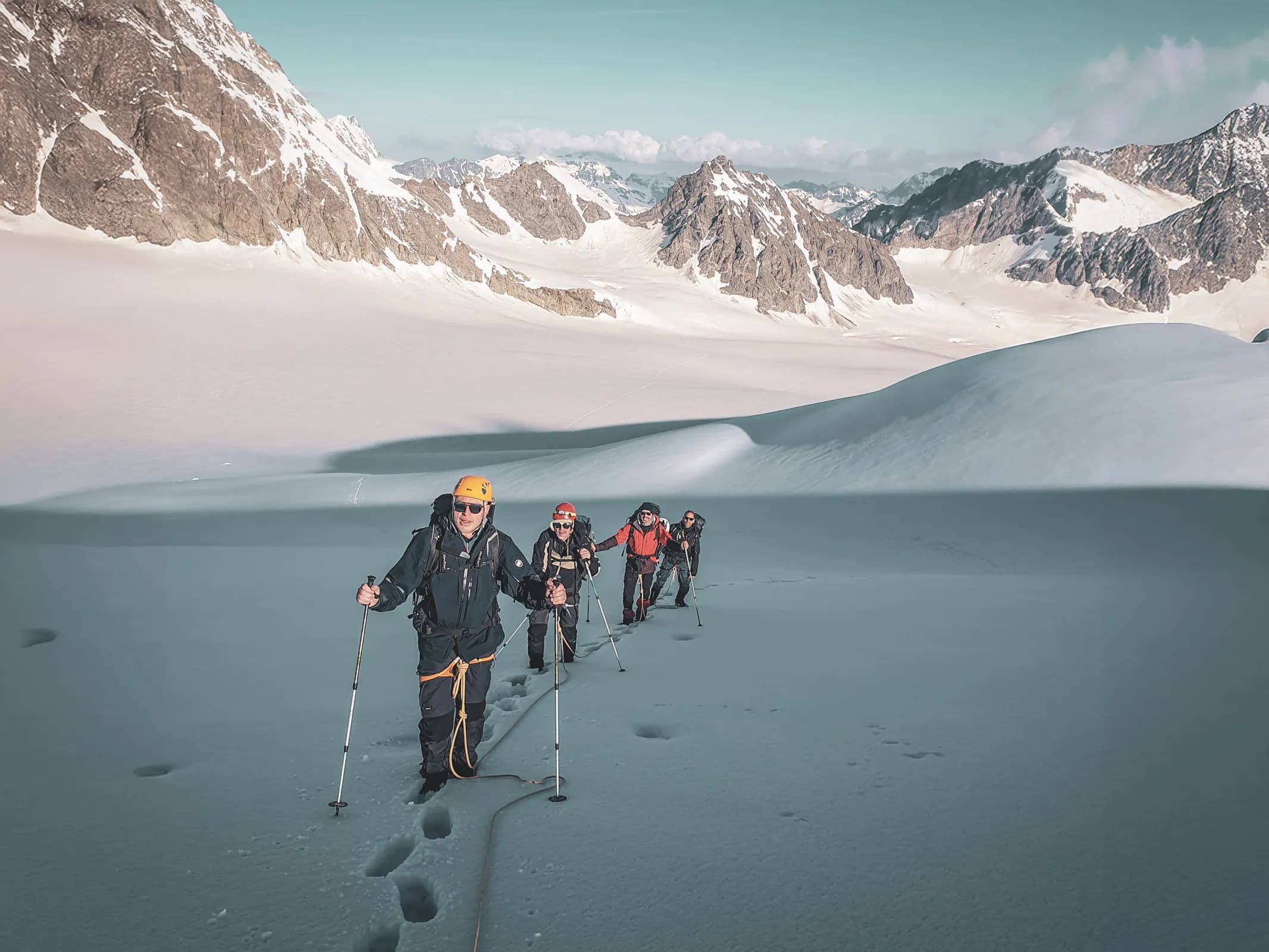Group of climbers advancing on a glacier, surrounded by majestic Alpine peaks.