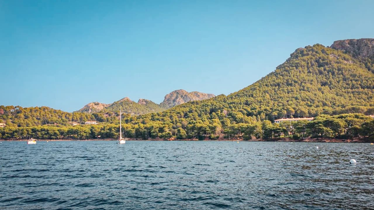 Sun-drenched coves in the Balearic Islands, peaceful sailing boats and lush green mountains in the background.