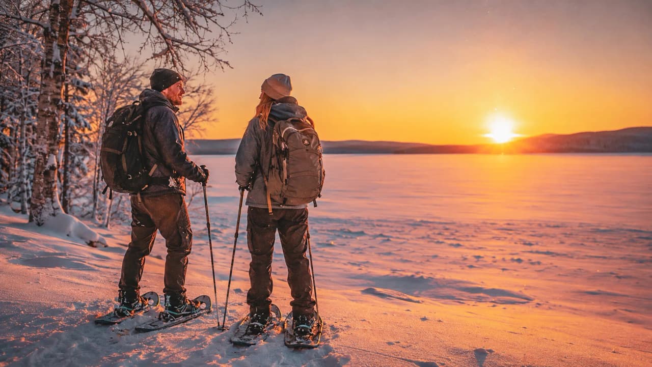 Two snowshoe hikers are admiring a stunning sunset over a snow-covered landscape.