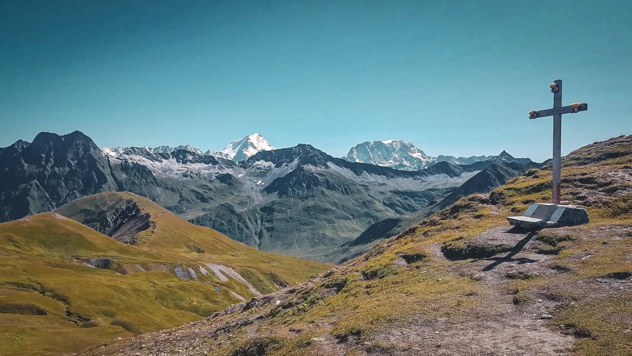 An enchanting panorama of mountains, a bench and a cross overlooking majestic glaciers.