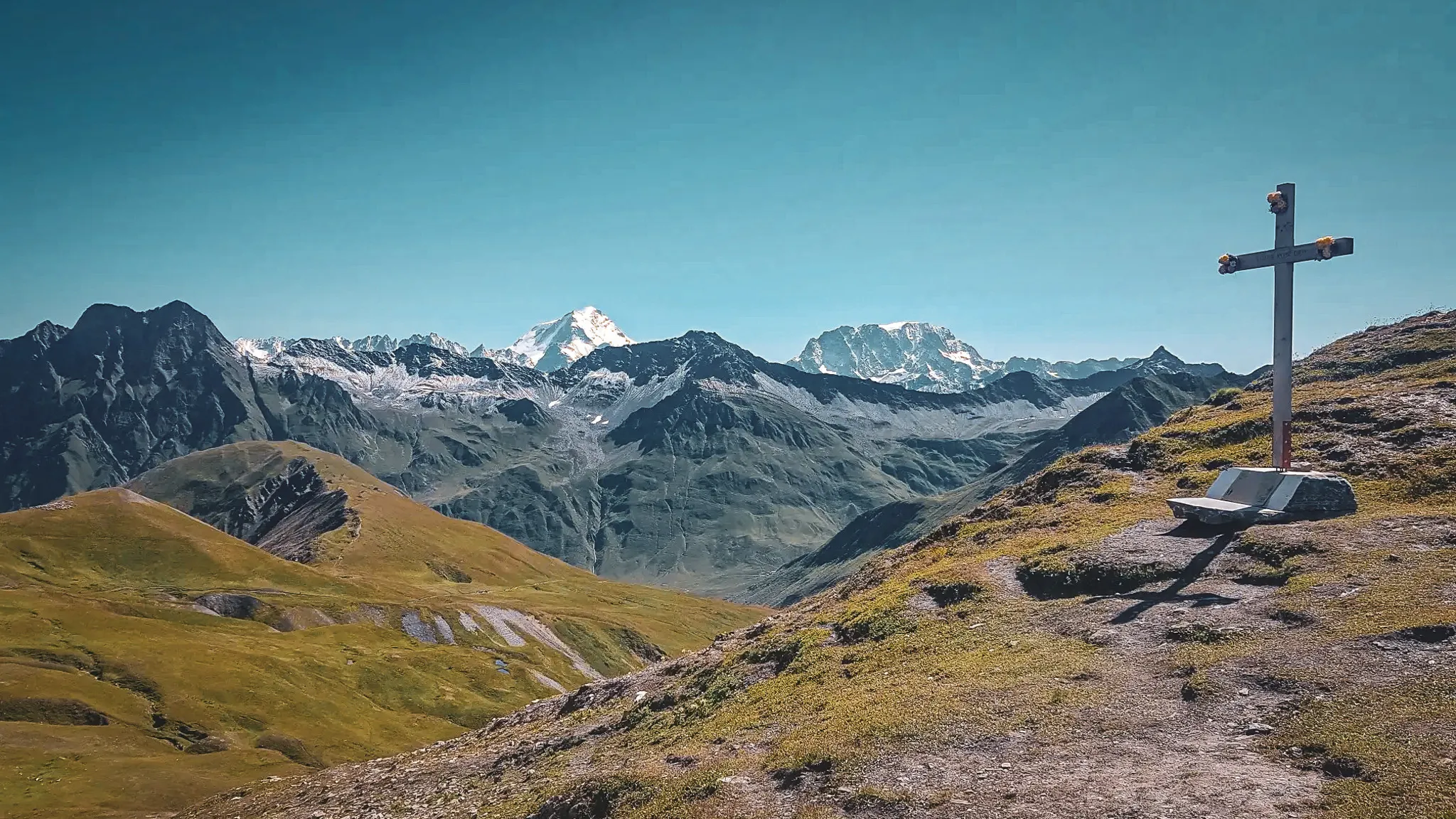 An enchanting panorama of mountains, a bench and a cross overlooking majestic glaciers.