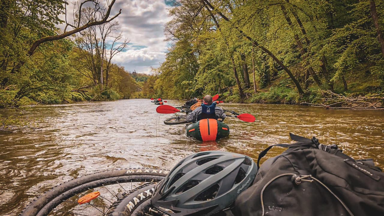 A group of kayakers on the Lesse, surrounded by lush green forest, with a peaceful, adventurous atmosphere.