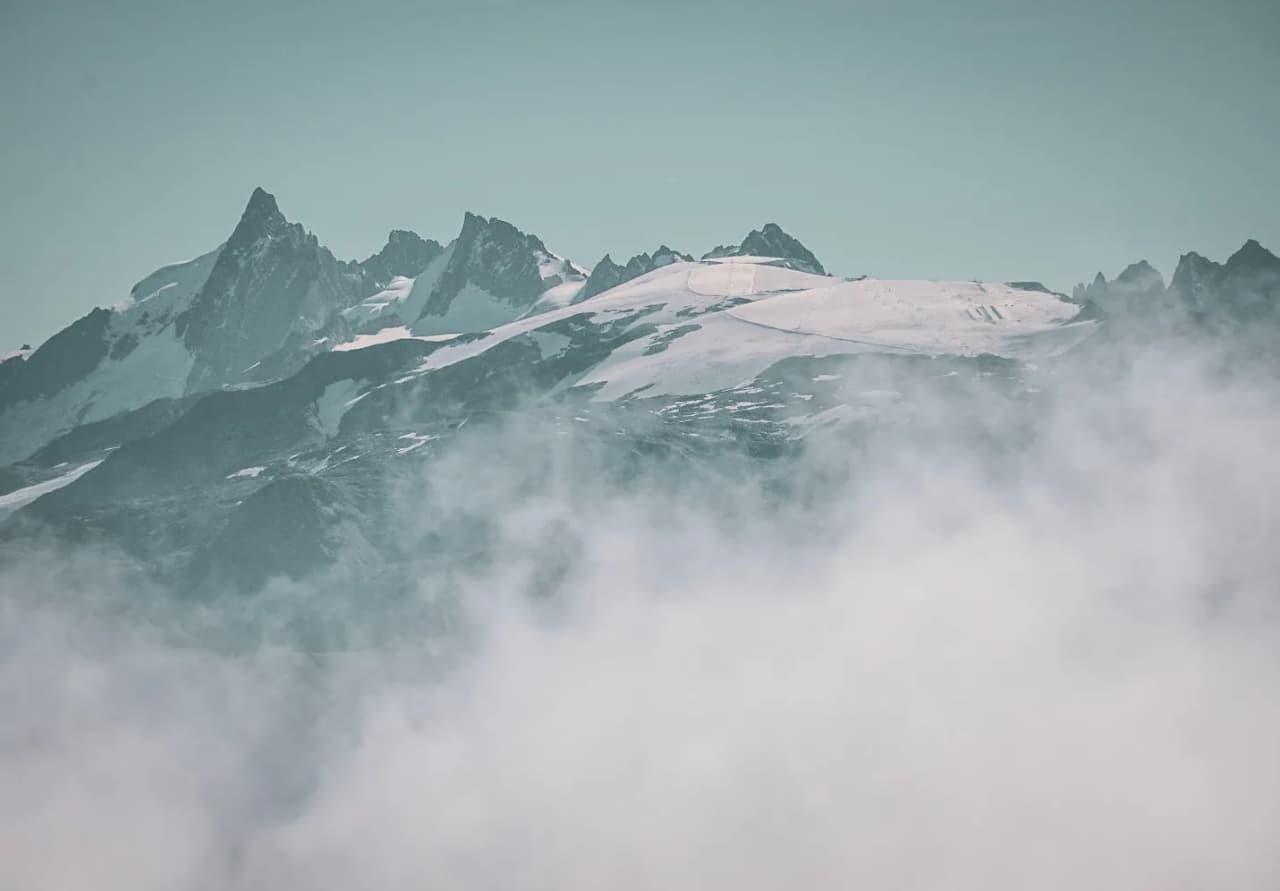 Montagnes enneigées sur fond de ciel clair, enveloppées de brume.