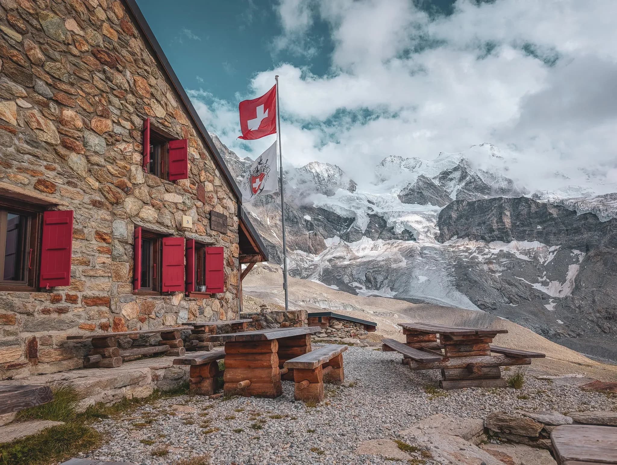 Stone chalet with Swiss flag, facing majestic mountains, ideal for mountaineering.