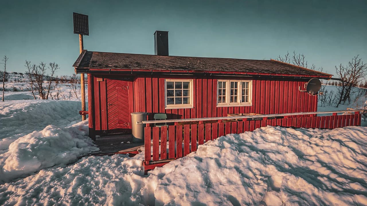 Échoppe rouge au milieu de la neige, refuge chaleureux en Laponie norvégienne.