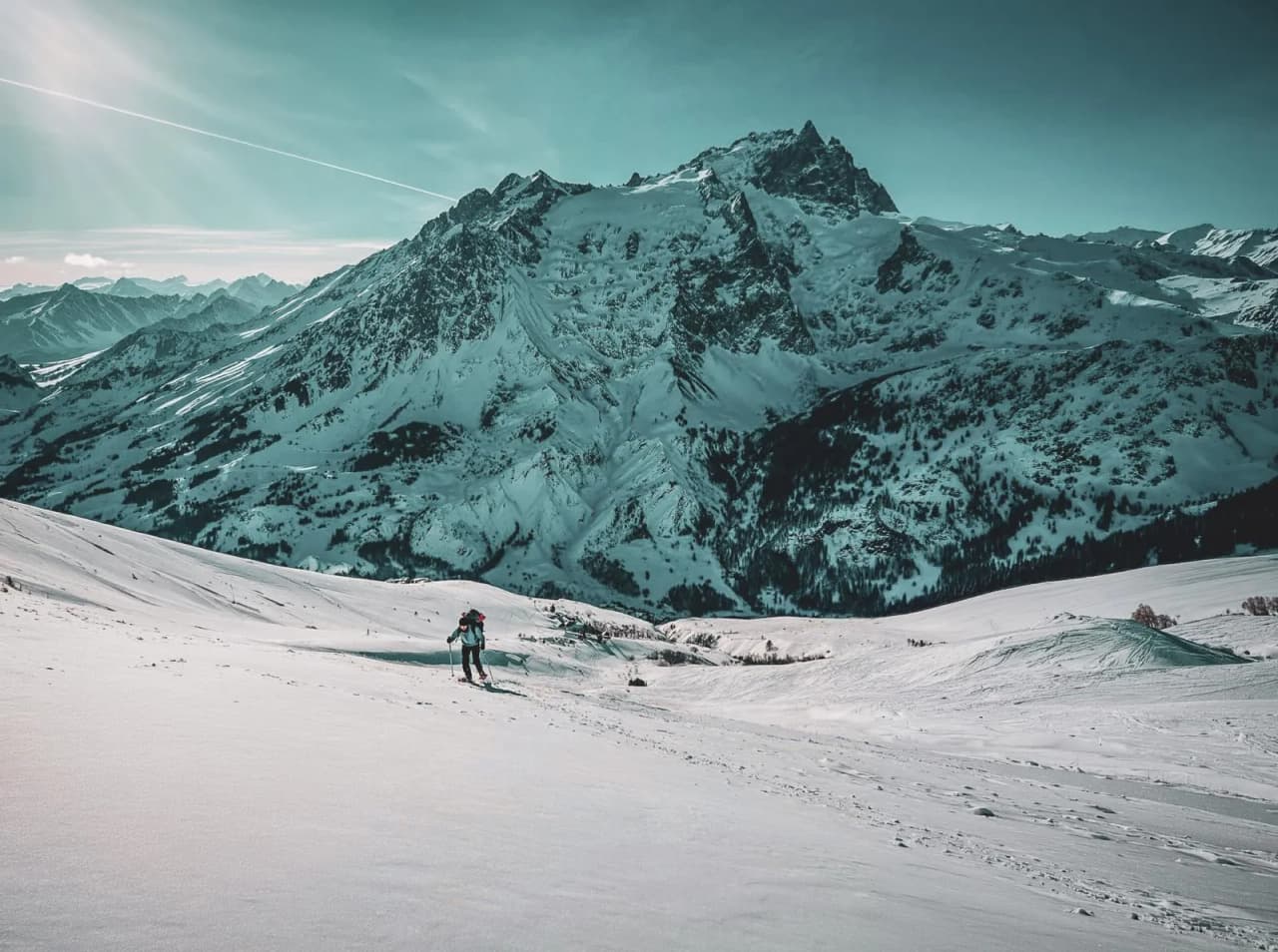 Een persoon op sneeuwschoenen doorkruist een besneeuwd landschap met de majestueuze Meije op de achtergrond.