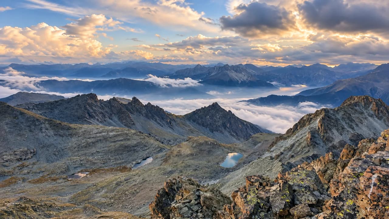 A panoramic view of the majestic mountains of Monte Viso, amidst clouds and golden light.