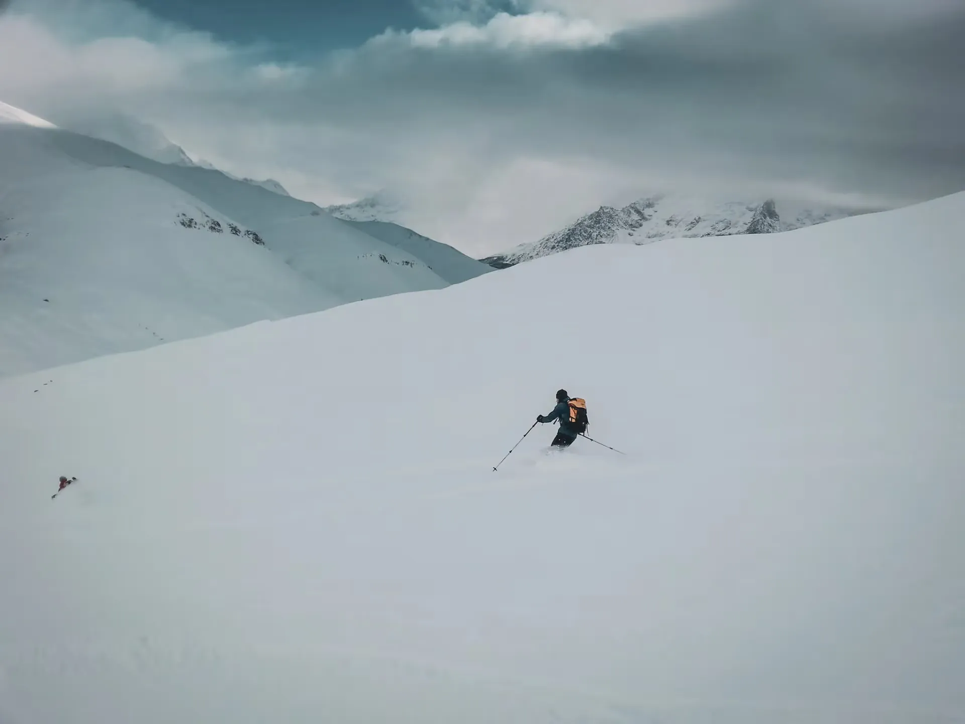 Skier in full descent on a vast snowfield, majestic mountains in the background.